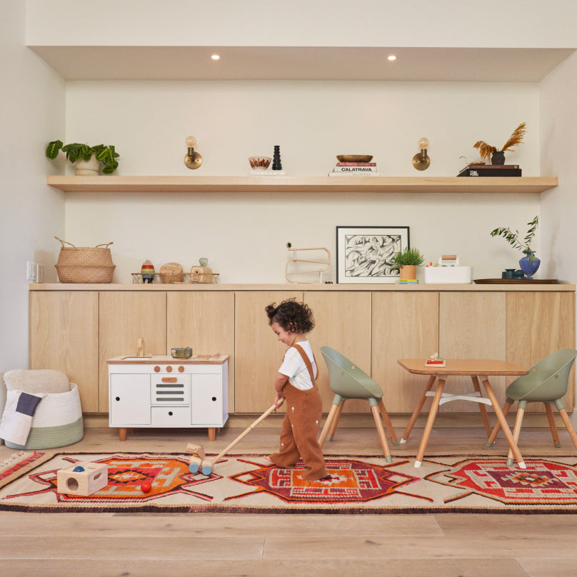 A child playing with a wooden push-toy shaped like a dog in a room filled with Lalo furniture and toys.