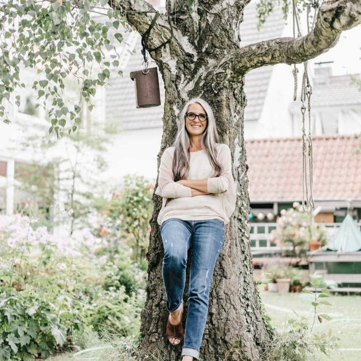 A woman leans against a tree in a backyard