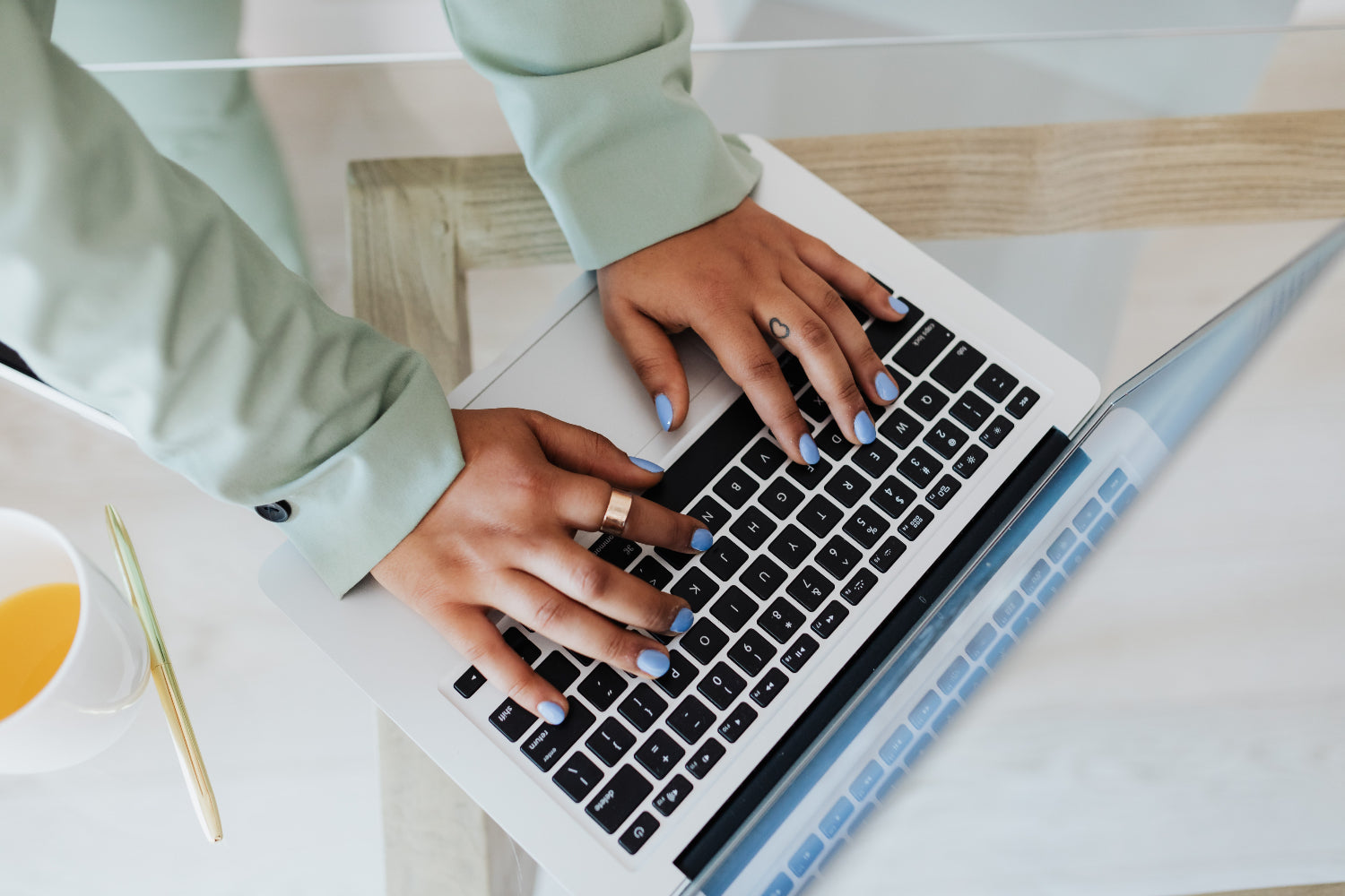 Bird’s eye view of hands typing on laptop keyboard, wearing mint green sweater and blue nail polish