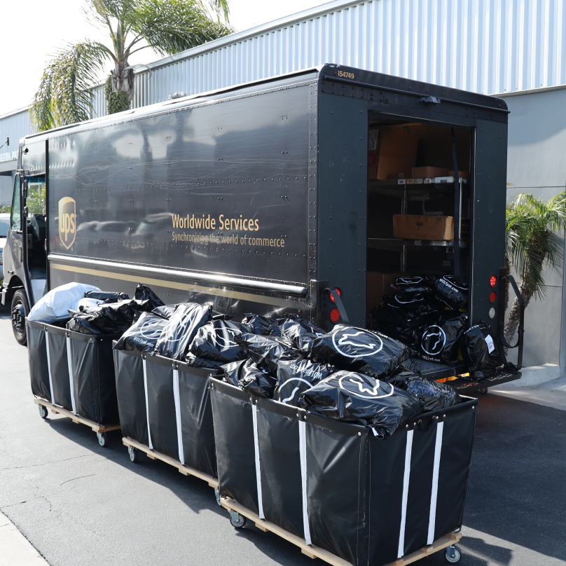 UPS delivery truck open in the back, beside three large shipping containers overflowing with packages from WOLFpak