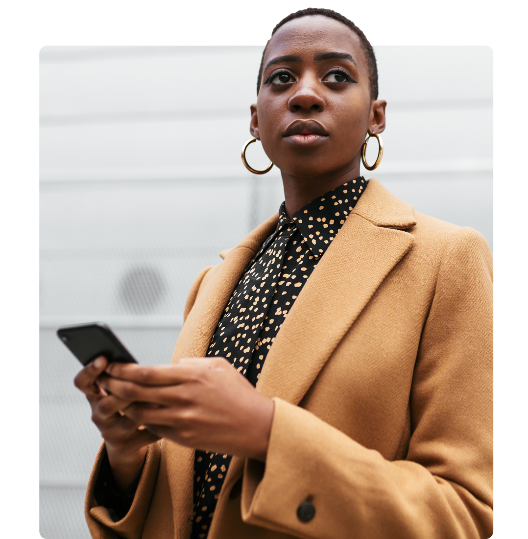 A Black woman in stylish professional clothes checks her phone.