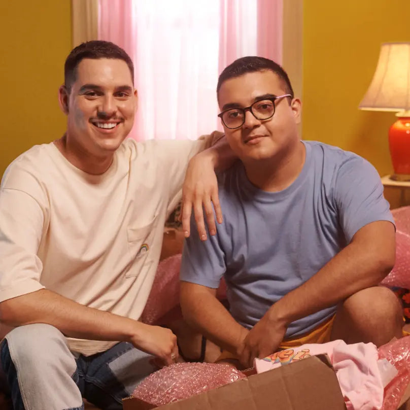 The two owners of Gay Pride apparel, sitting in a yellow room and smiling.