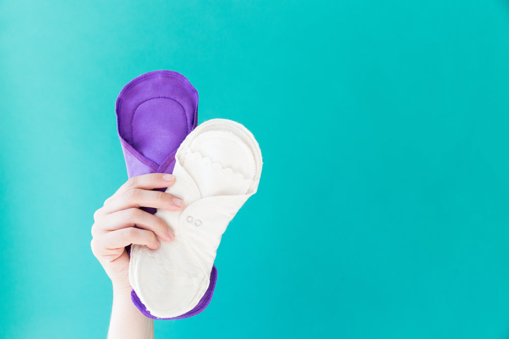 a hand holds up two reusable menstrual pads