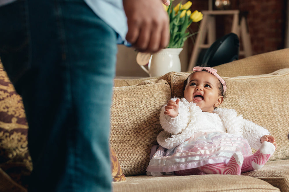 baby girl on couch lookingat dad smiling