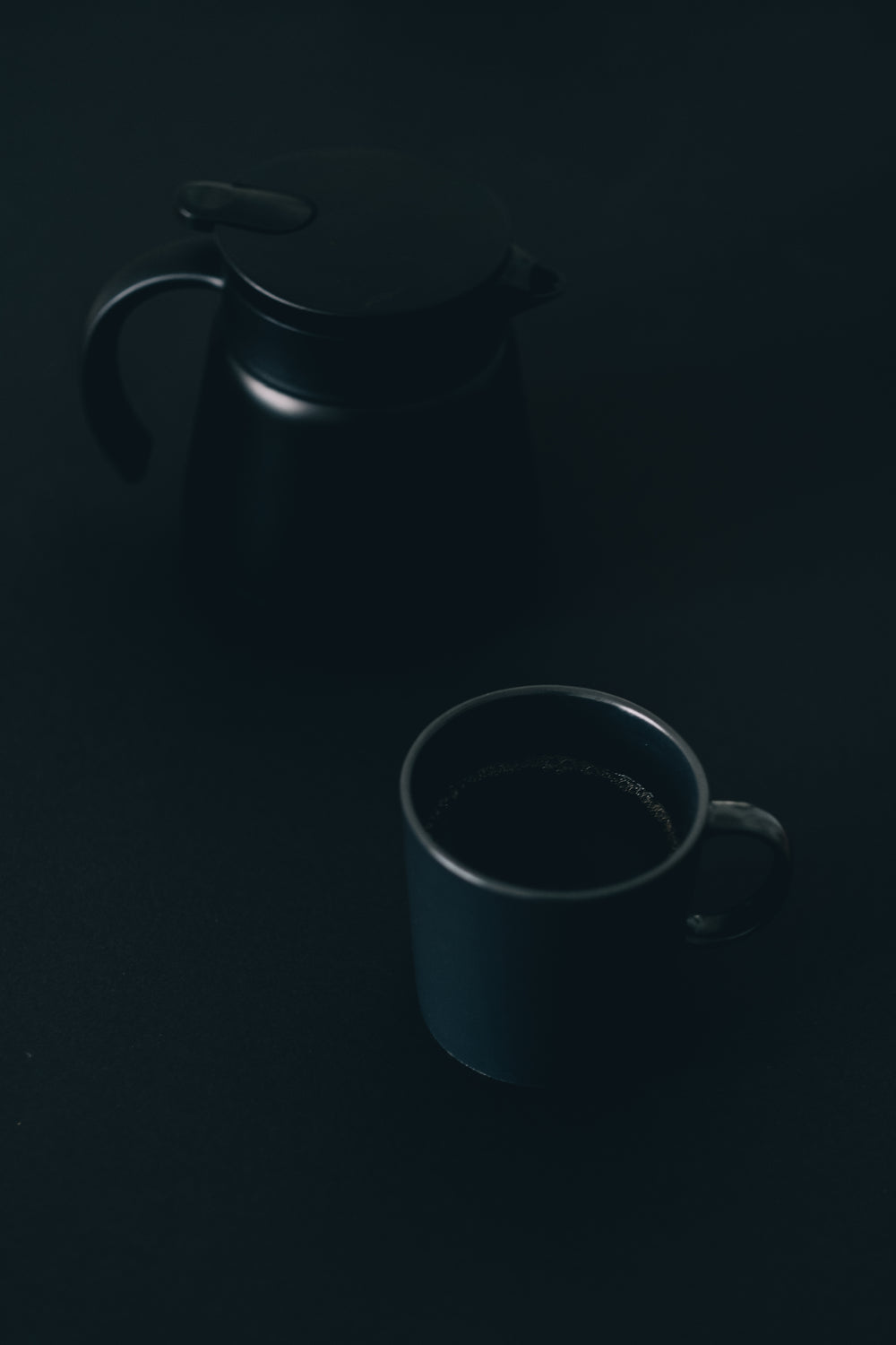 coffee mug and pot sitting on a black surface