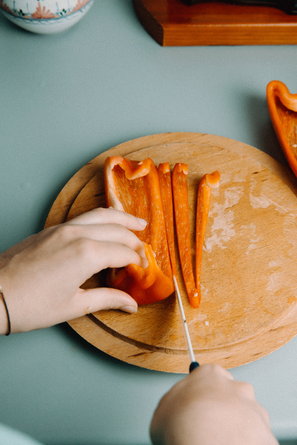 hands slice red pepper on wooden cutting board