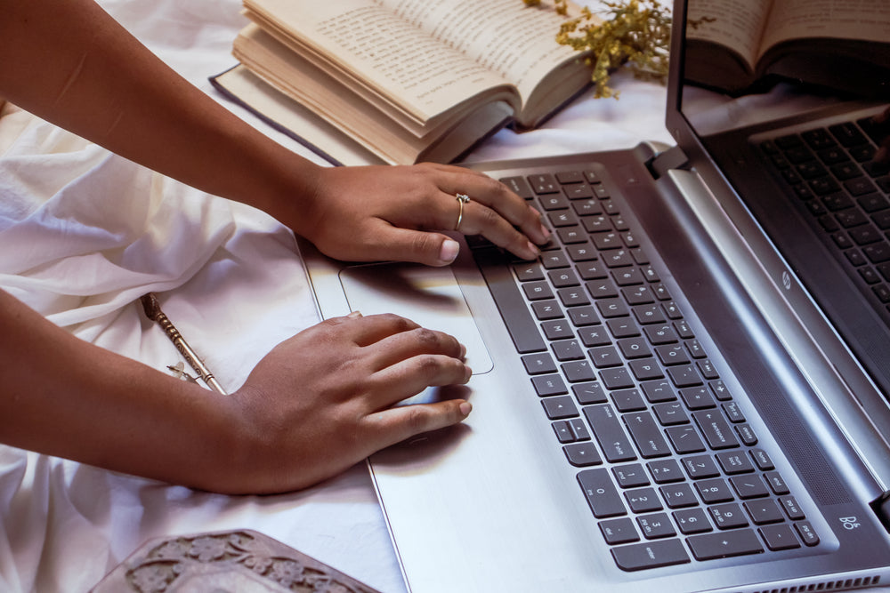 hands type on a laptop that is resting on a white cloth