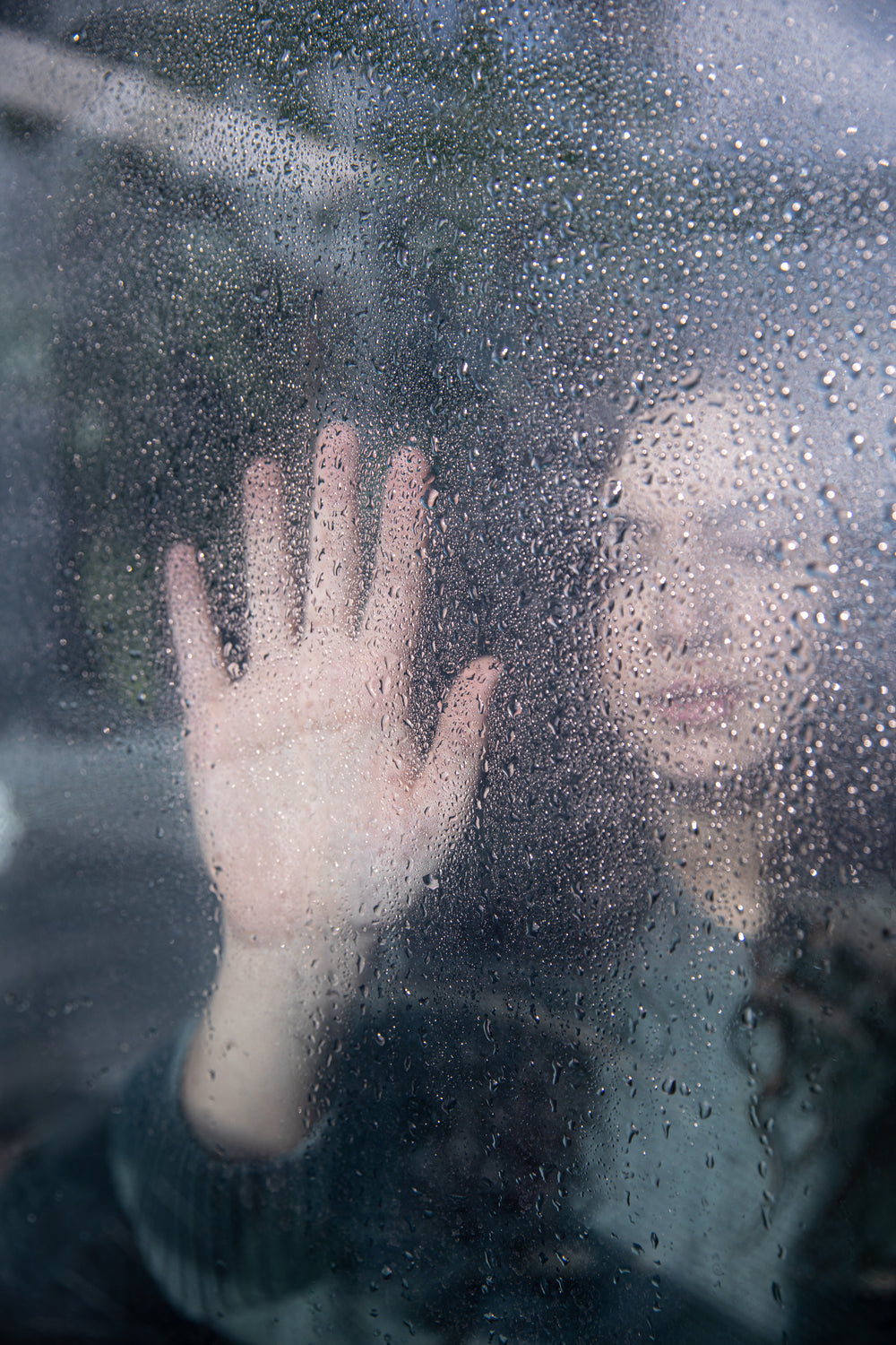 person holds their hand up to wet glass