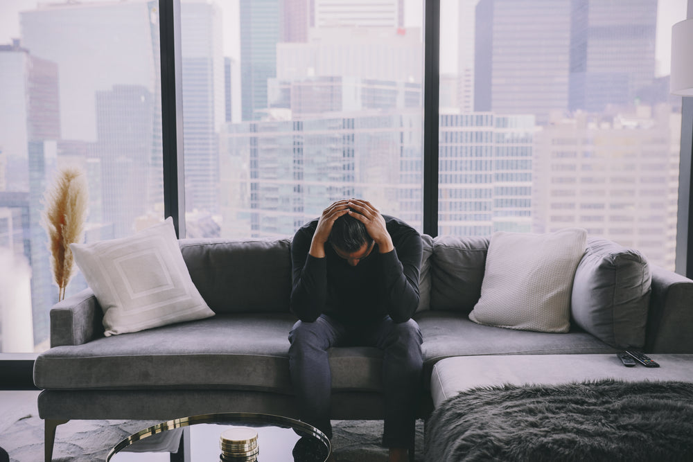 person holds their head while sitting on a couch