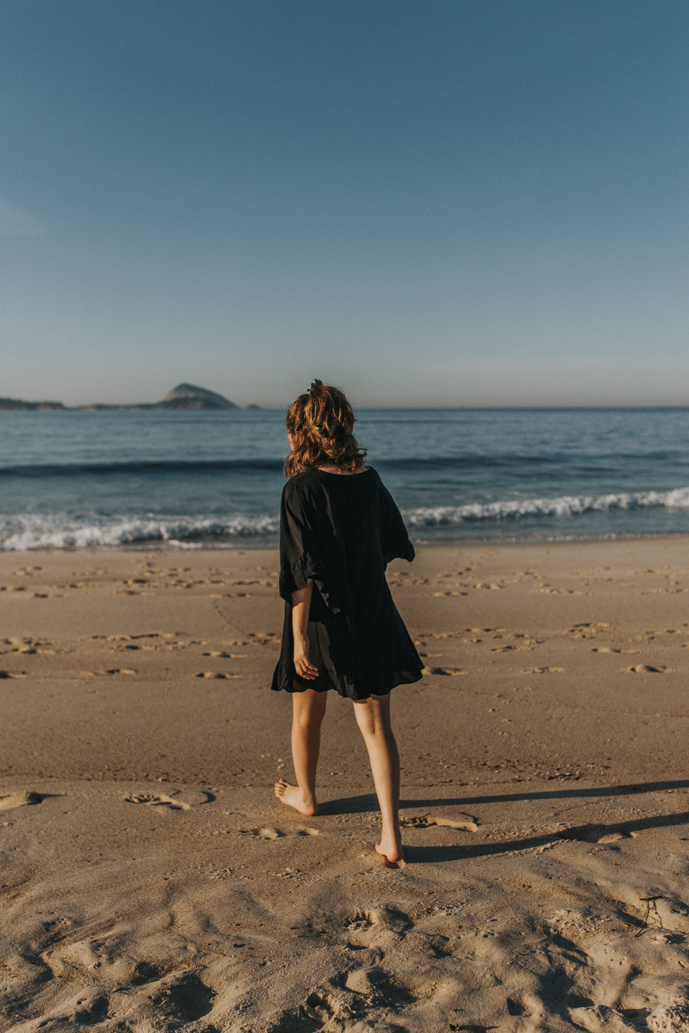 person in a black dress walks on the beach