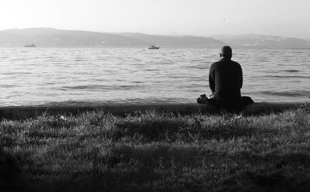 person sits looking out towards still water