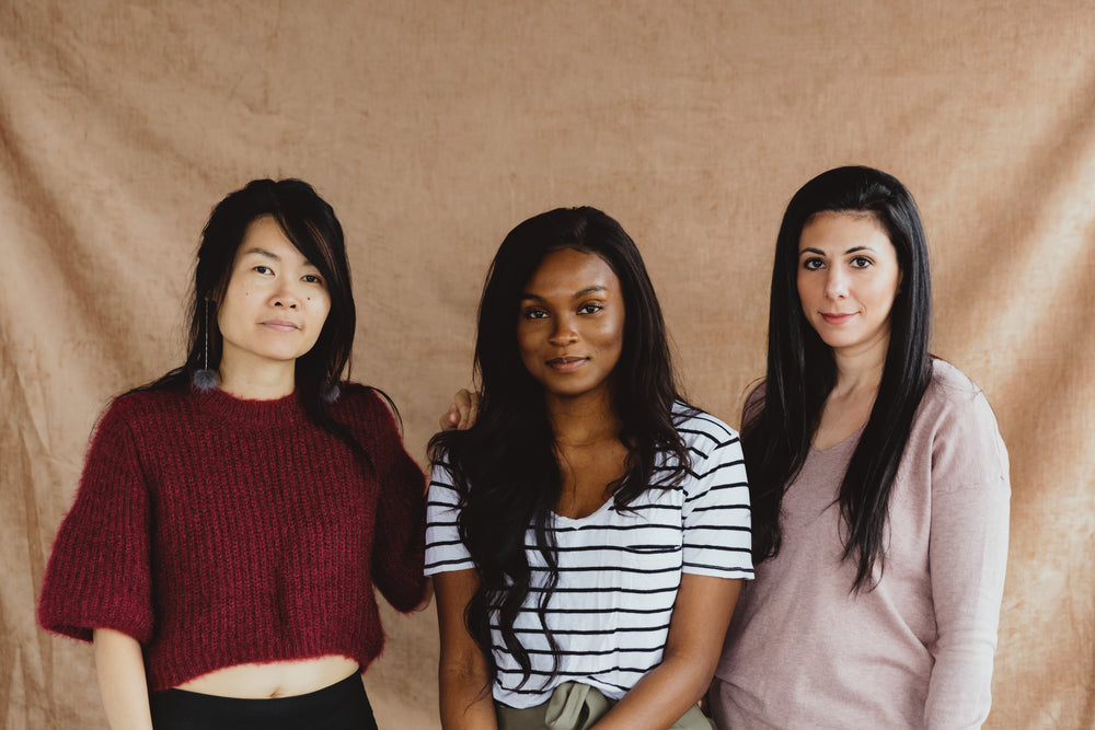 three woman stand in front of a pink backdrop