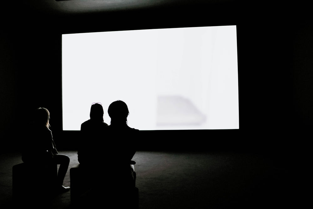 three woman watch a glowing white screen in a dark room