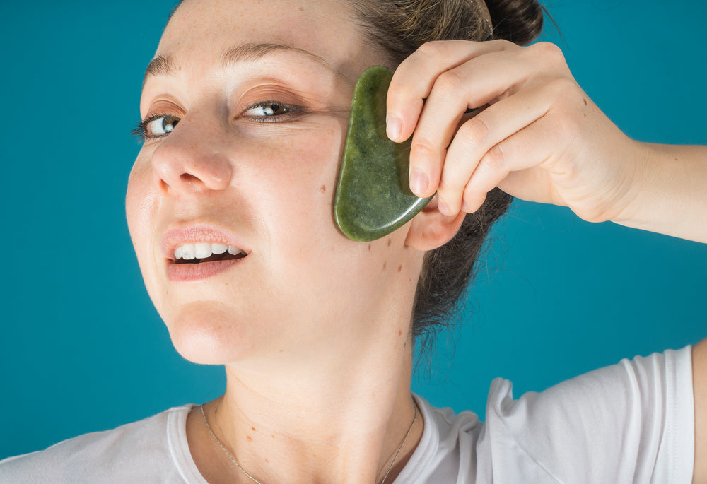 woman holds a jade face massager to her face