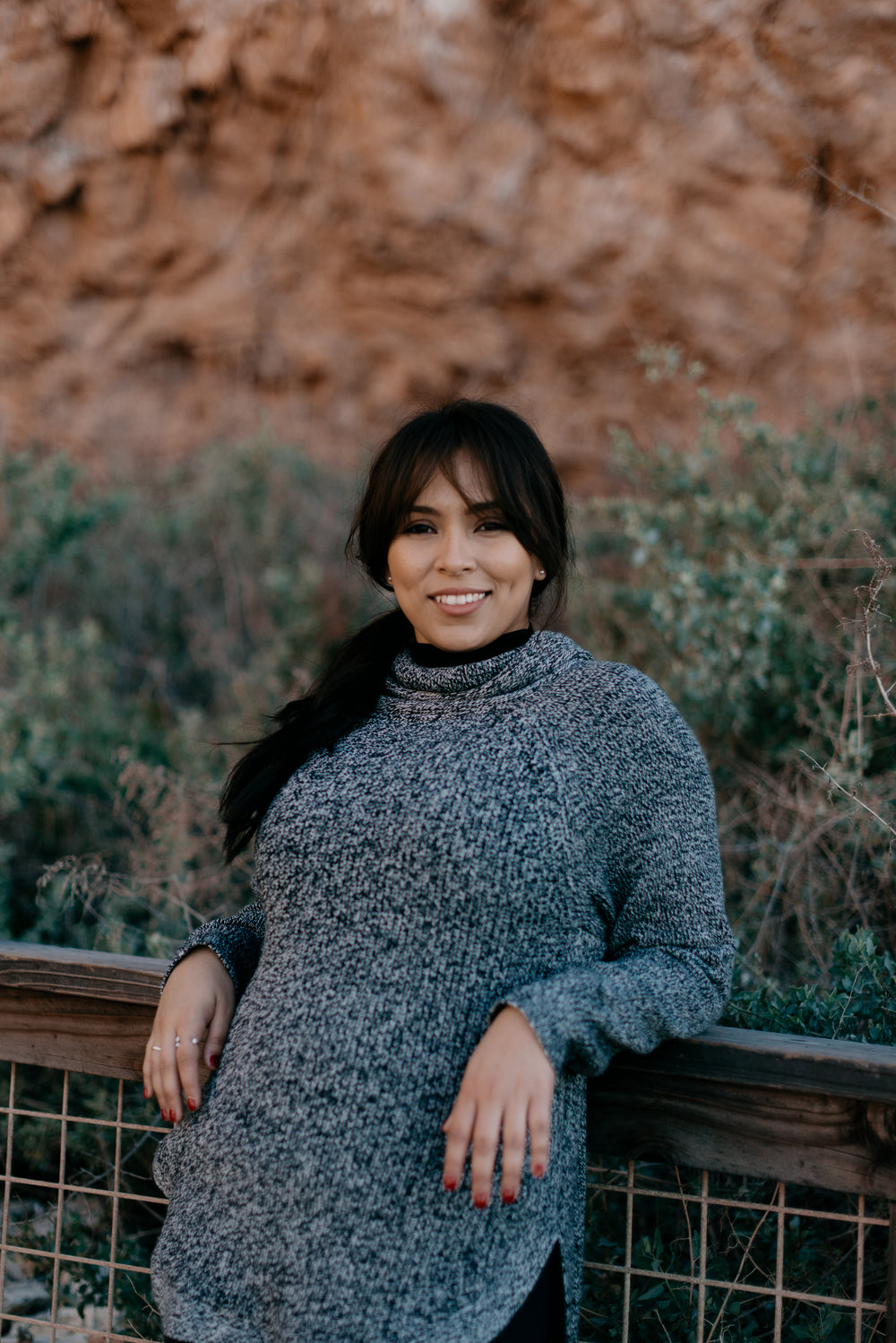 woman in grey sweater smiles and leans against a railing