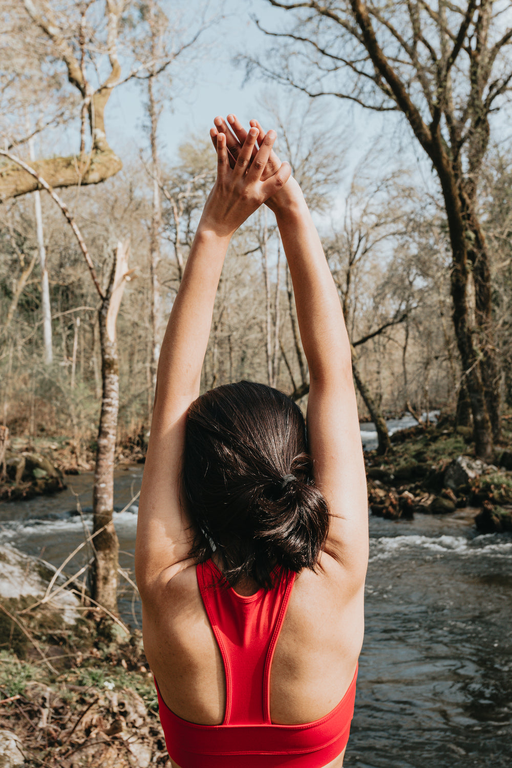 woman in vibrant red reaches arms up in a stretch outdoors