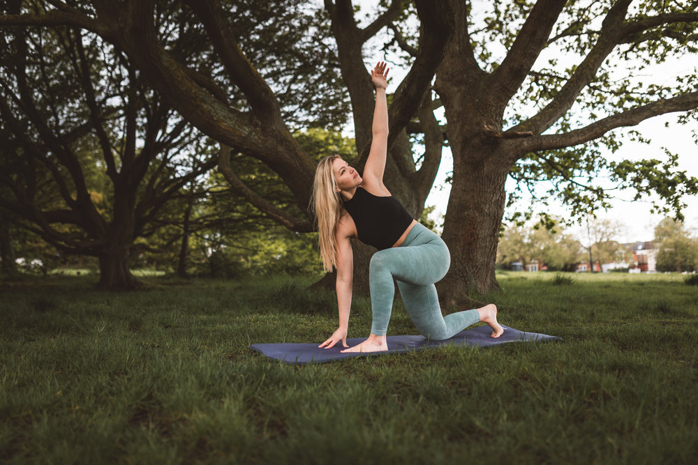 woman practices yoga under a large tree