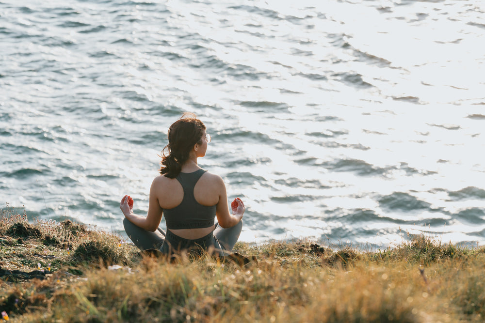 woman sits with her legs crossed facing the ocean