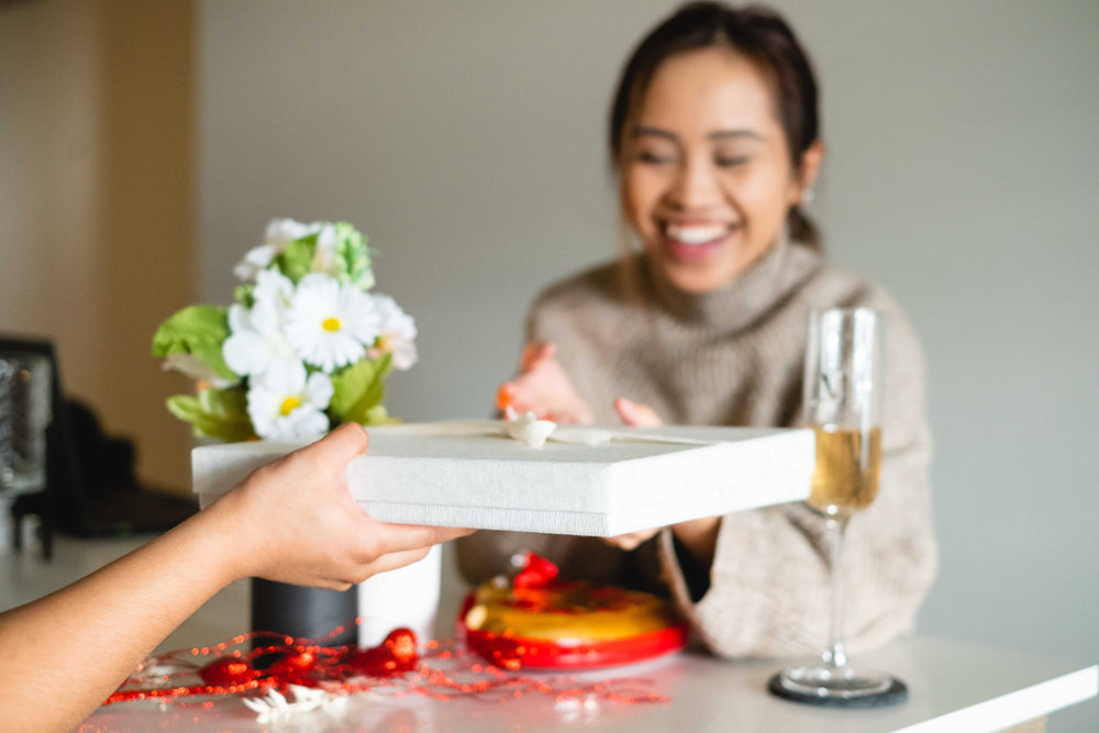 woman smiles as an arm reaches to give her a wrapped gift