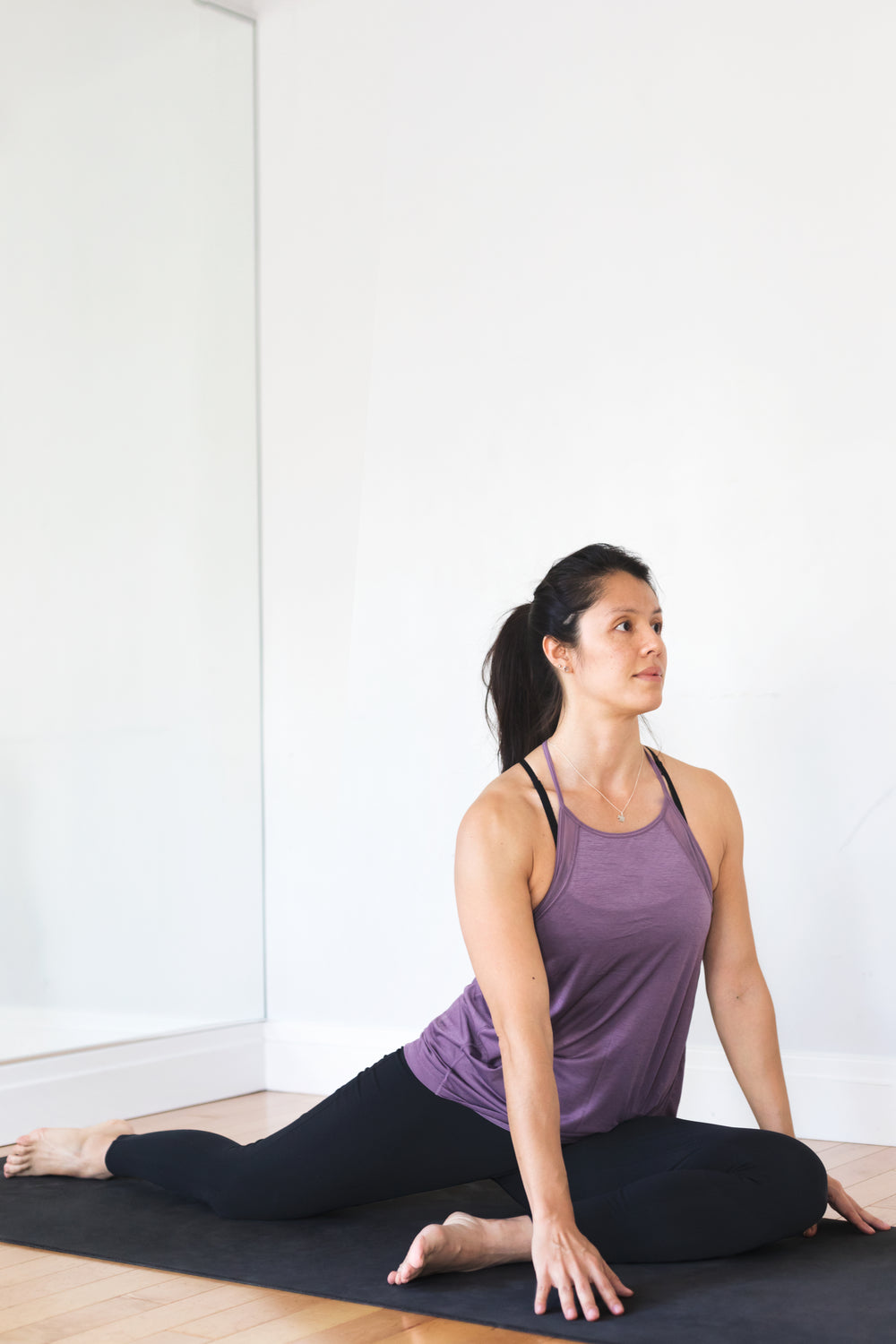 young woman doing yoga pose against white wall